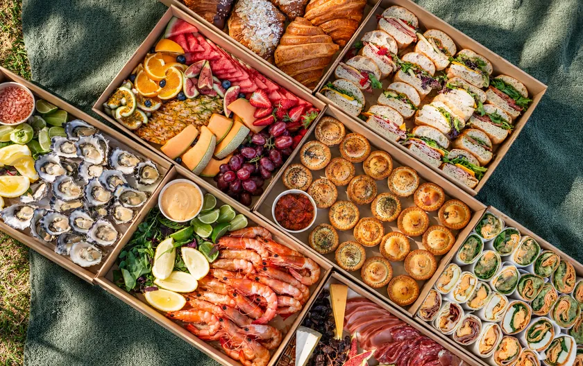 Catering boxes from above on the lawn: oysters, prawns, pies, croissants, wraps